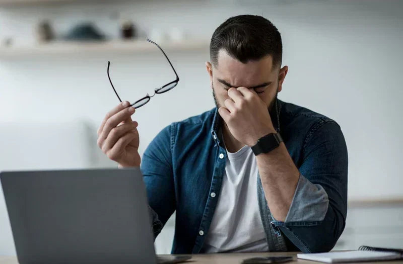 Man sitting in front of computer touching his eyes that appear to be dry